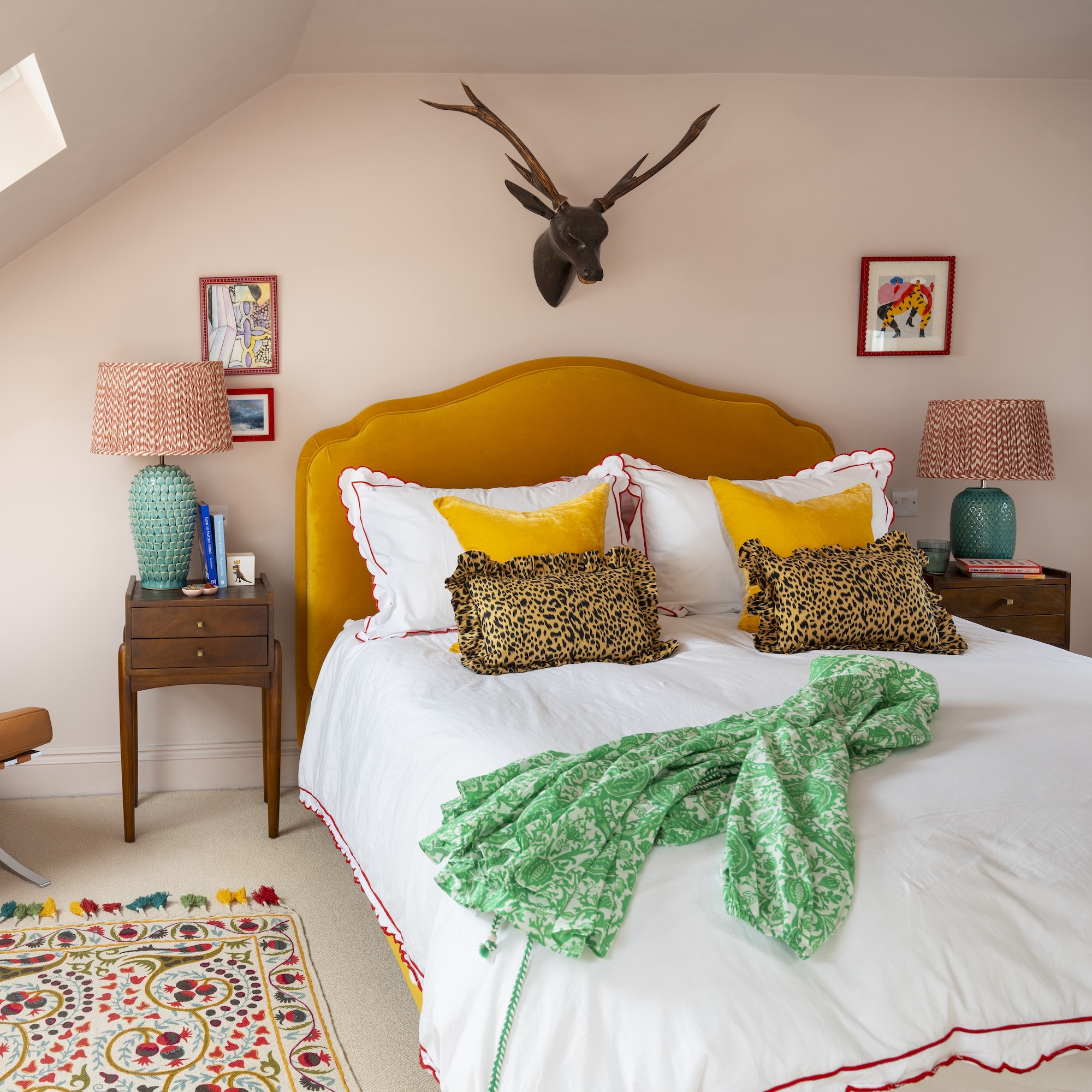 bedroom with pink walls, yellow upholstered headboard, stag head on wall, leopard print cushions and colourful rug