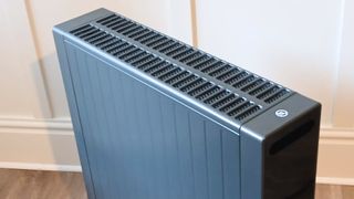 Close-up of a grey portable heater's vented top panel against a white panelled wall.