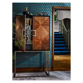 Green motif wallpaper in dining room with mid century modern wooden cabinet and blue stairs in the background
