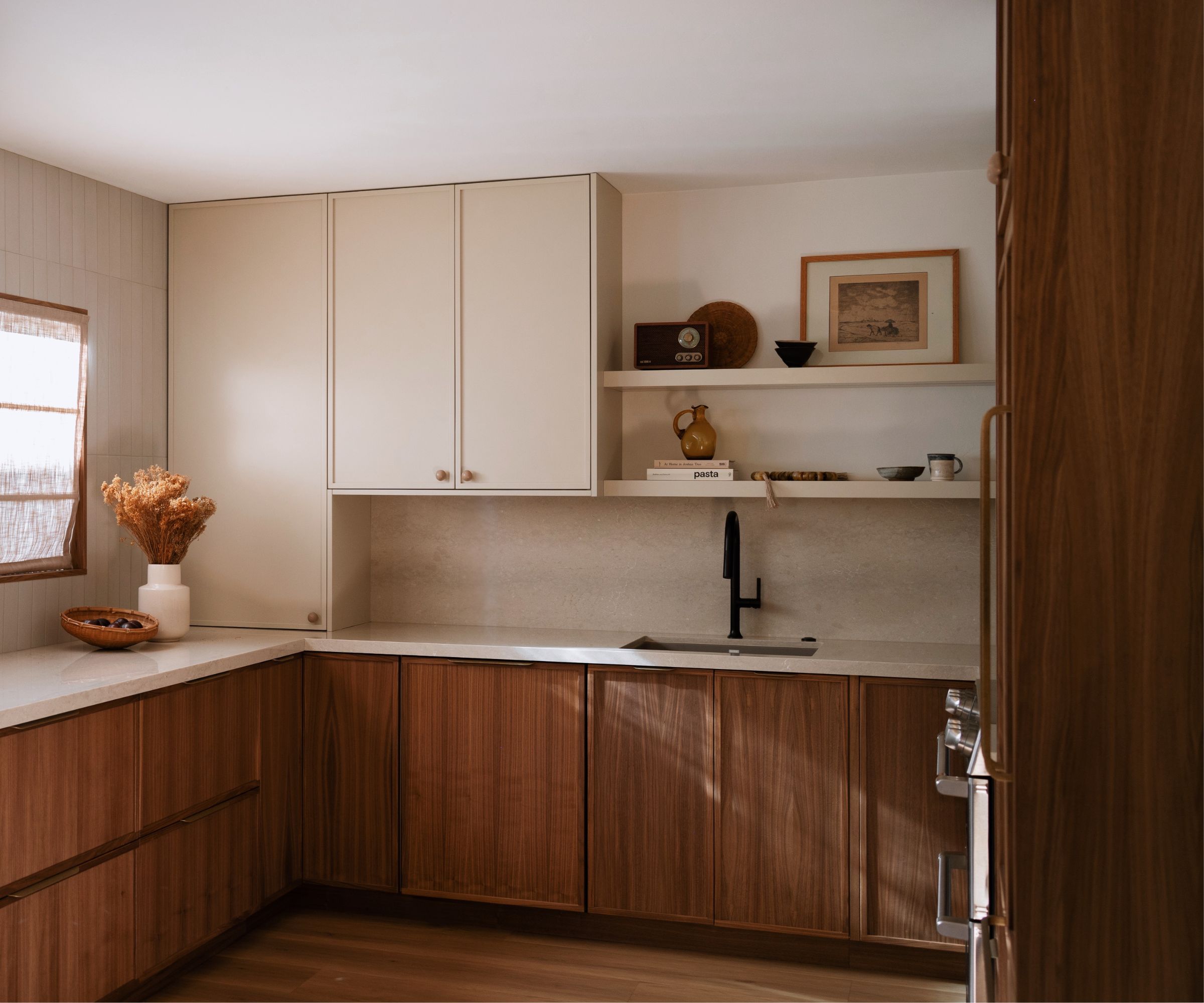 A neutral kitchen with white walls and upper cabinets, dark wood lower cabinets, and open shelving displaying art and decor