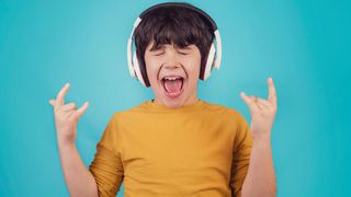 Child wearing a yellow t-shirt in front of a blue background throws up the rock horns
