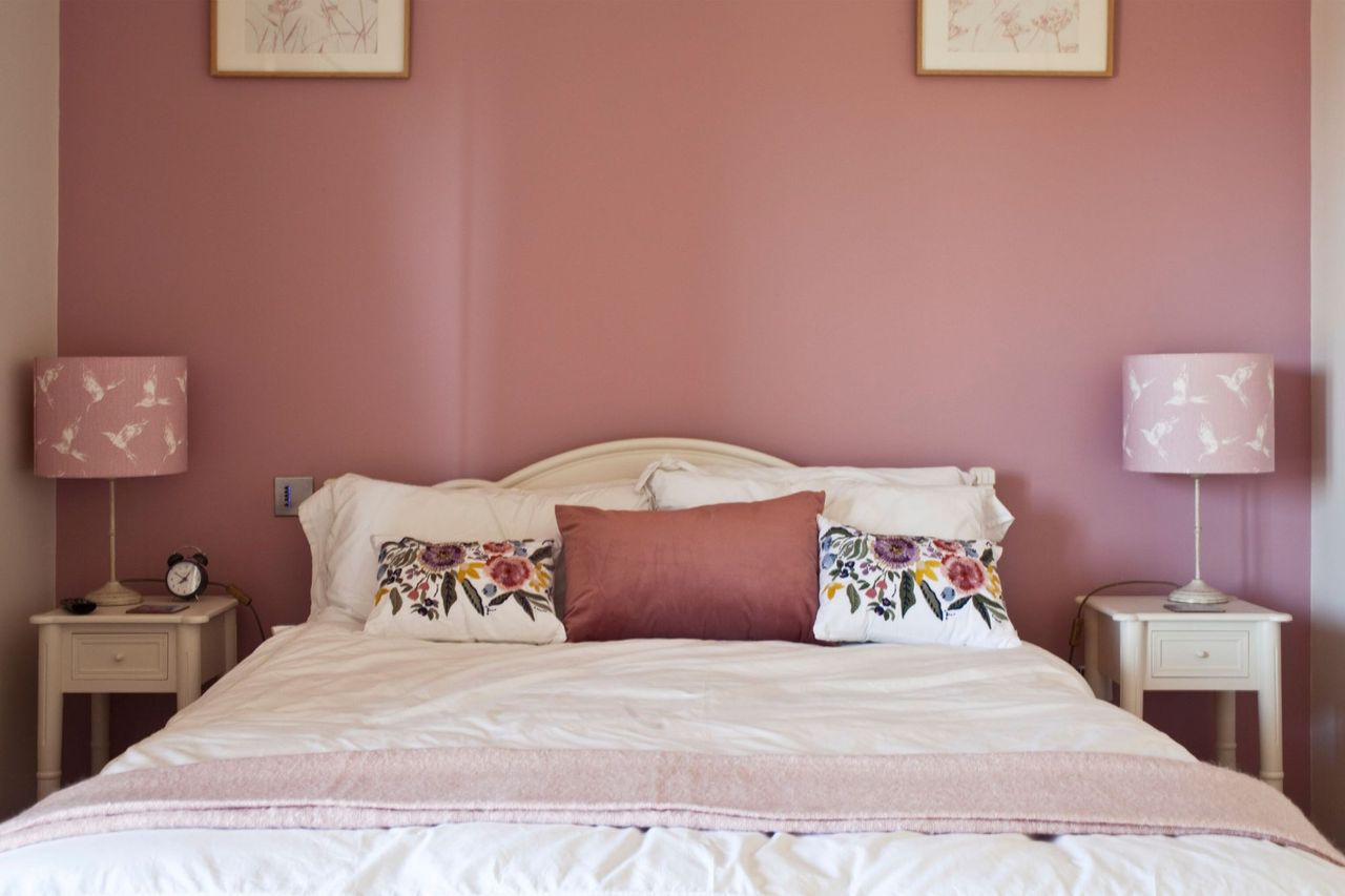 A blush pink bedroom with large double bed with cushions