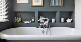 dark grey bathroom with storage alcoves behind a bathtub