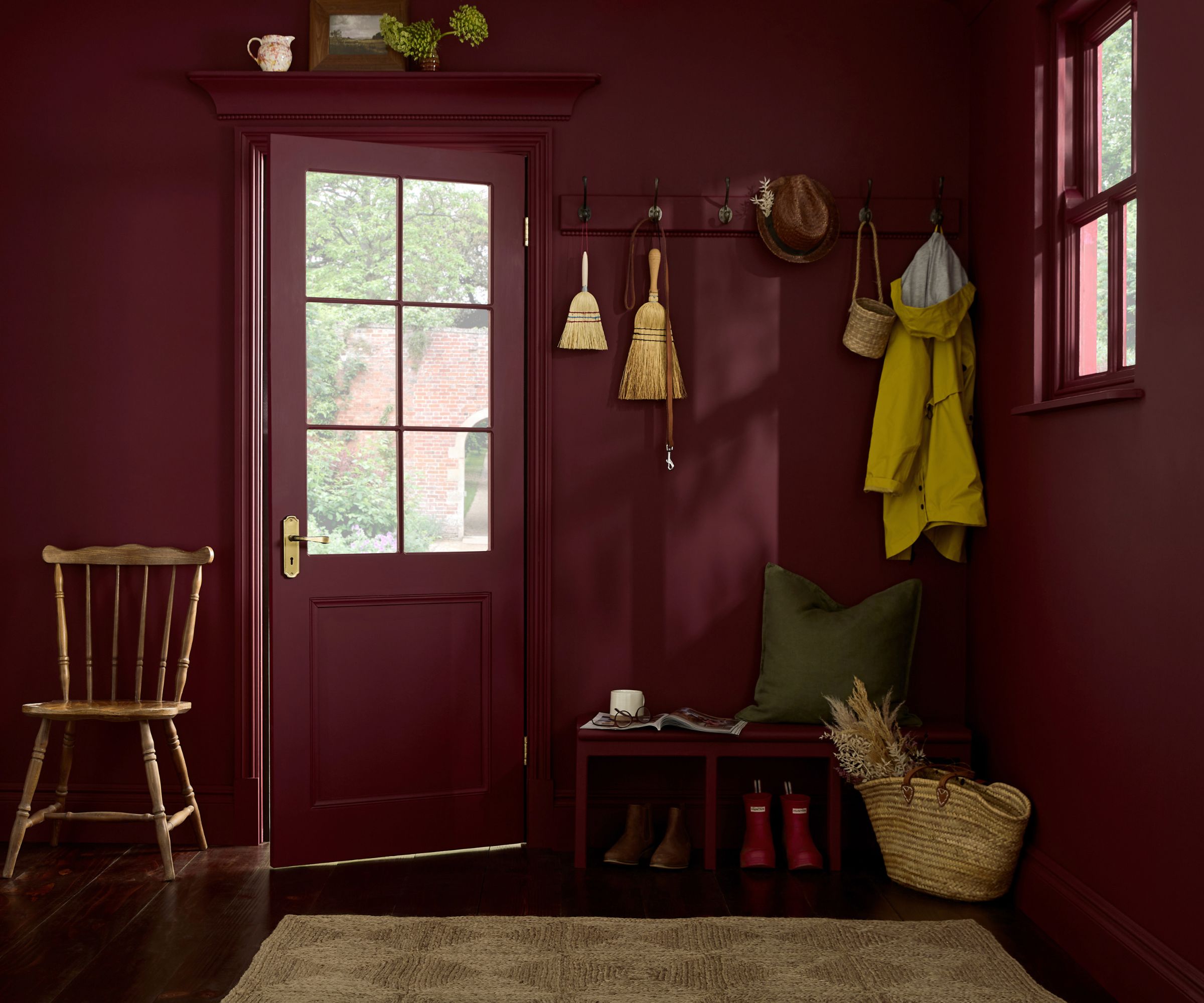 Dark red color-drenched mudroom with hooks holding coats and bags, bench with shoes and a wooden chair
