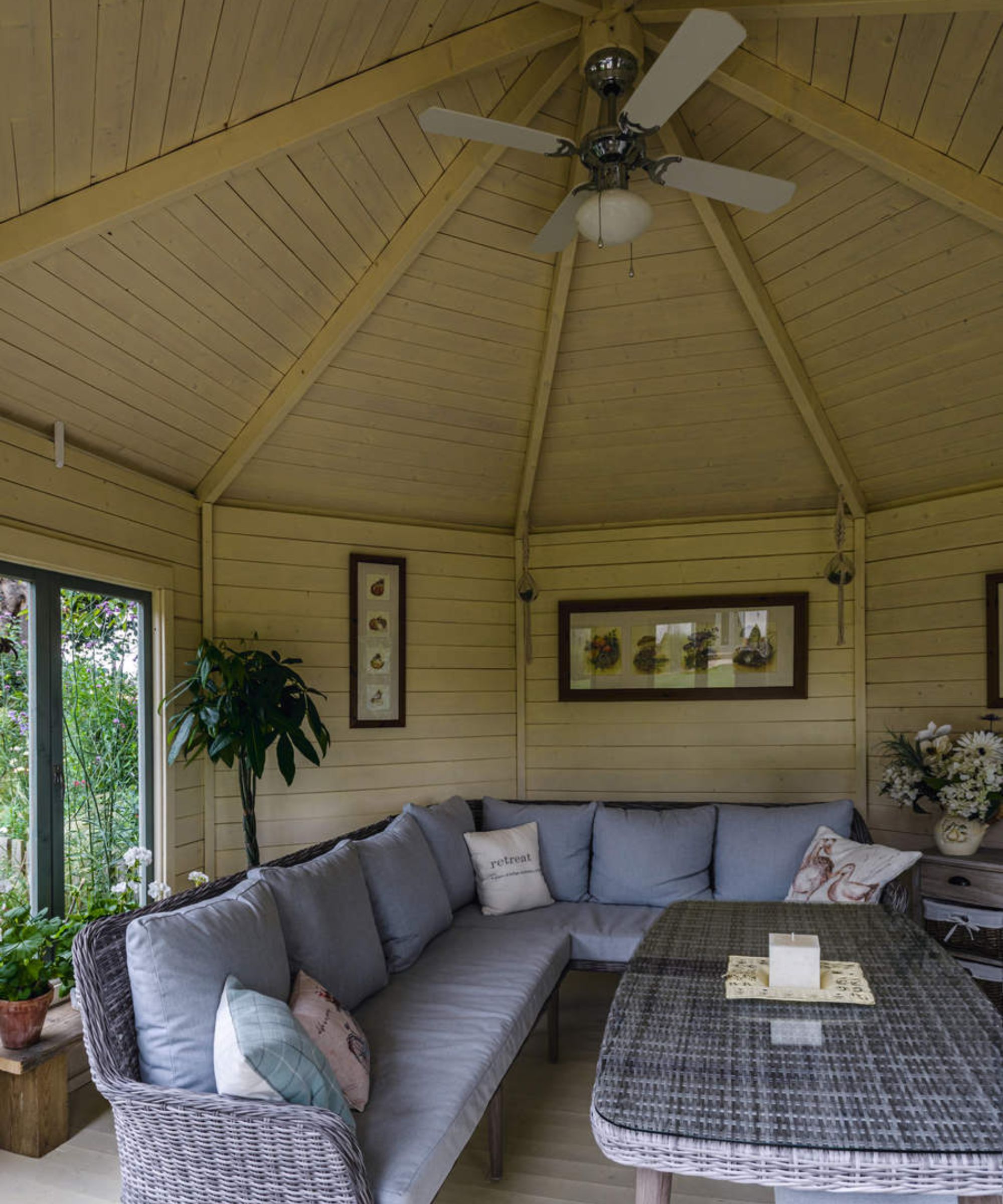 A sun room with a large L shaped rattan sofa and a ceiling fan
