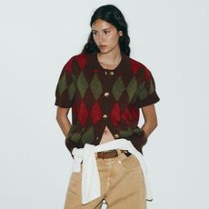 model wears short sleeved argyle sweater and brown jeans.