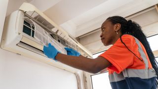 black Female technician service open air conditioner indoor for checking and repairing, Air conditioner service indoors. Air conditioner cleaning technician she opened the front cover and took out the filters and washed it