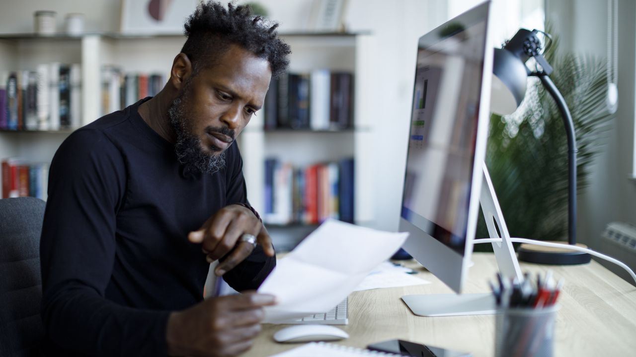 A man looks concerned as he looks at paperwork while sitting at his desk.