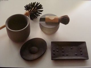 Brown ceramic bathroom accessories featuring a rectangular and an oval soap bar holder, a toilet brush, a bowl and a powder brush on a brush holder photographed on a grey surface