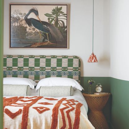 A bedroom with two-tone painted walls in white and green, a patterned upholstered headboard and a framed bird print hung above the bed