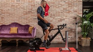 A man rides a bike, which is connected to an Elite Suito trainer and Elite Rizer, in a living room