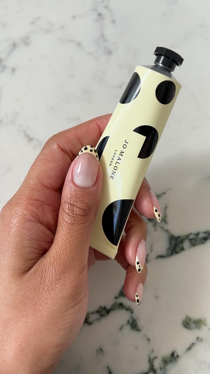 Cream and black dot French tip holding Joe Maron hand cream