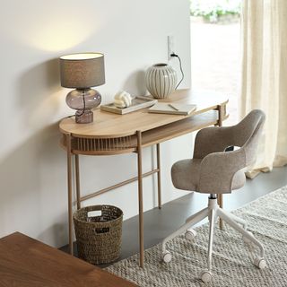 A curved EGELEV desk from JYSK in a home office with a table lamp and decorative items on top