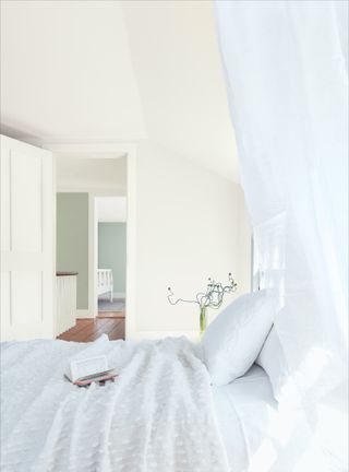 white bedroom with view to landing, white walls, white bedding, vase with stems, landing has pale sage green walls, wooden floorboards