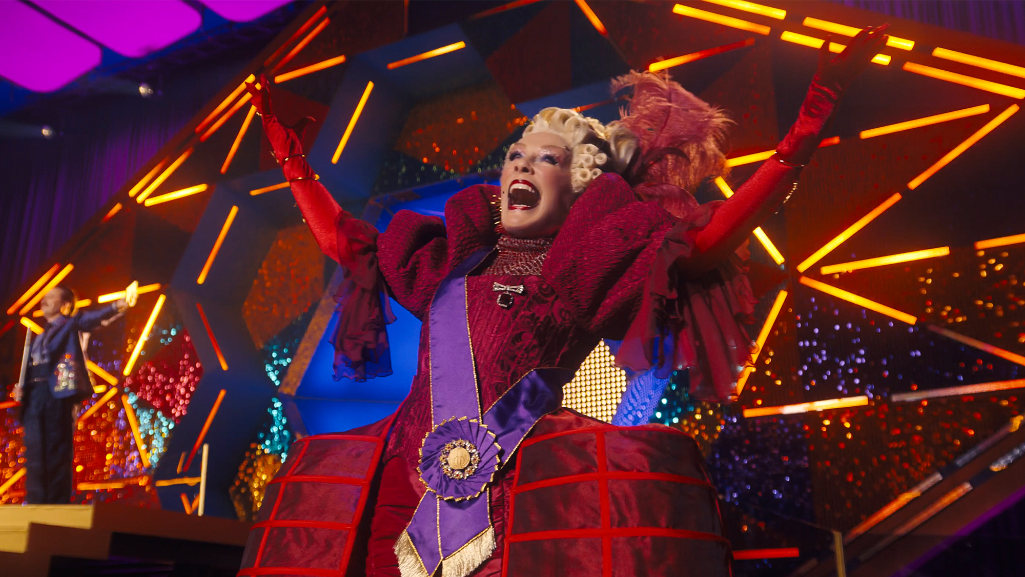 Glenn Close in a red dress, making a wild gesture with her arms in Sunrise on the Reaping