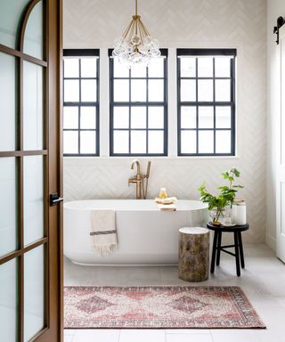 A rolltop bath beneath a window with an oriental rug instead of a bath mat