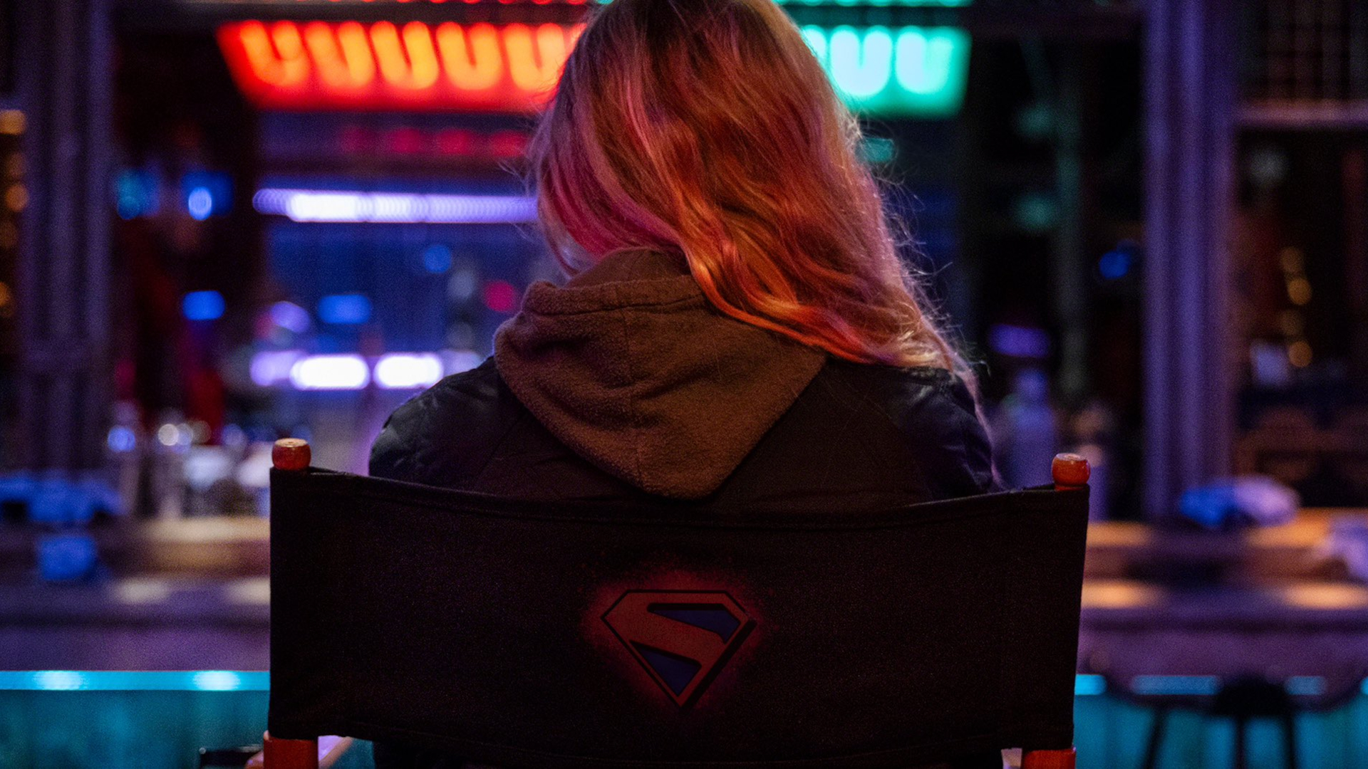 a blonde haired girl sitting in a director's chair with her back to us
