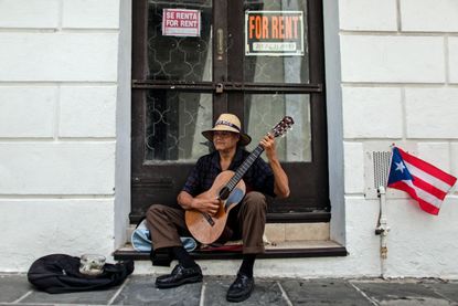 A man plays his guitar while he begs for money in front of a closed down business in Old San Juan, Puerto Rico