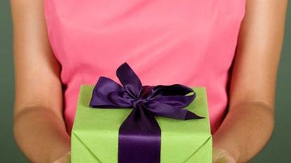 woman in pink dress holding gift wrapped in green with purple ribbon