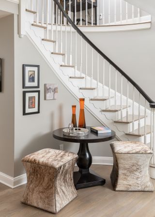 Curved staircase with side table and stools at base and artwork on wall