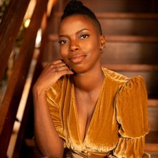 A portrait of Sasheer Zamata, sitting on a staircase.