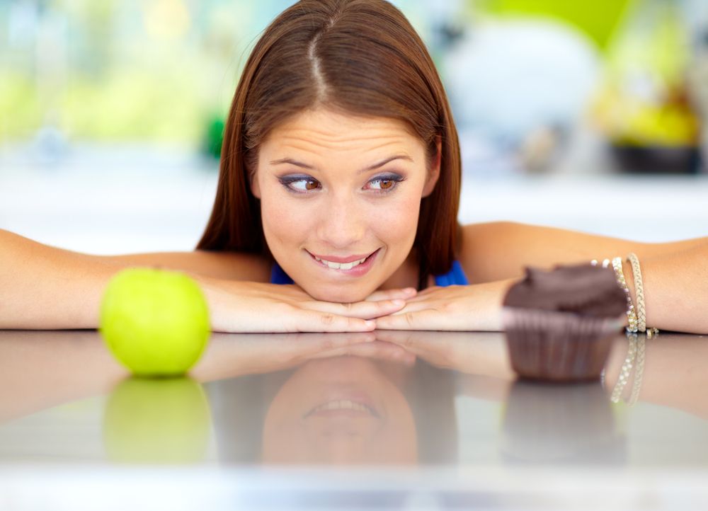 A woman decides between eating an apple or a cupcake