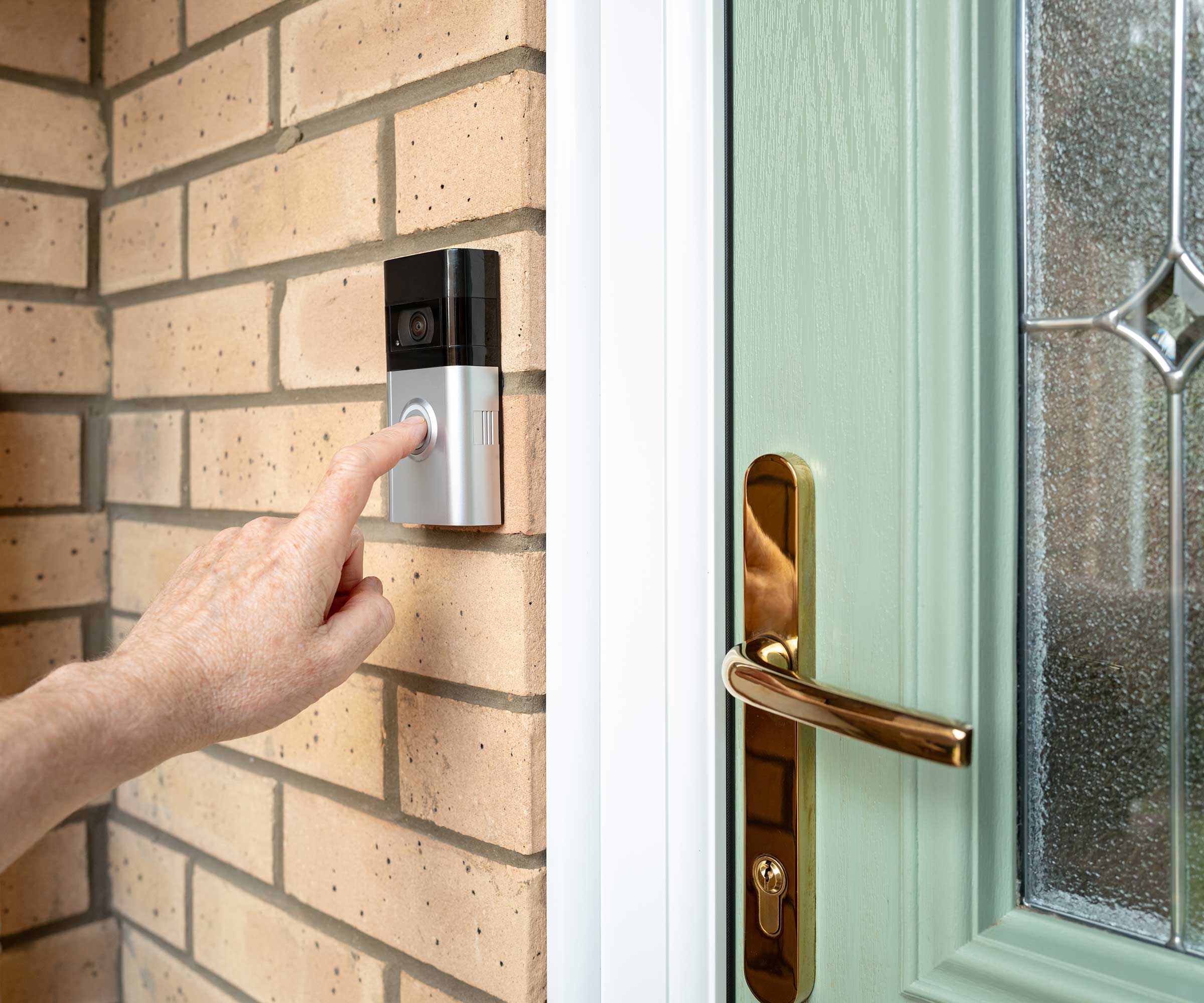 person pressing the button on a video doorbell on a house with a pale green front door