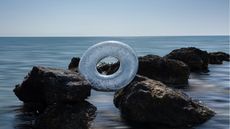 An inflatable ring is perched on rocks on the ocean's shore.