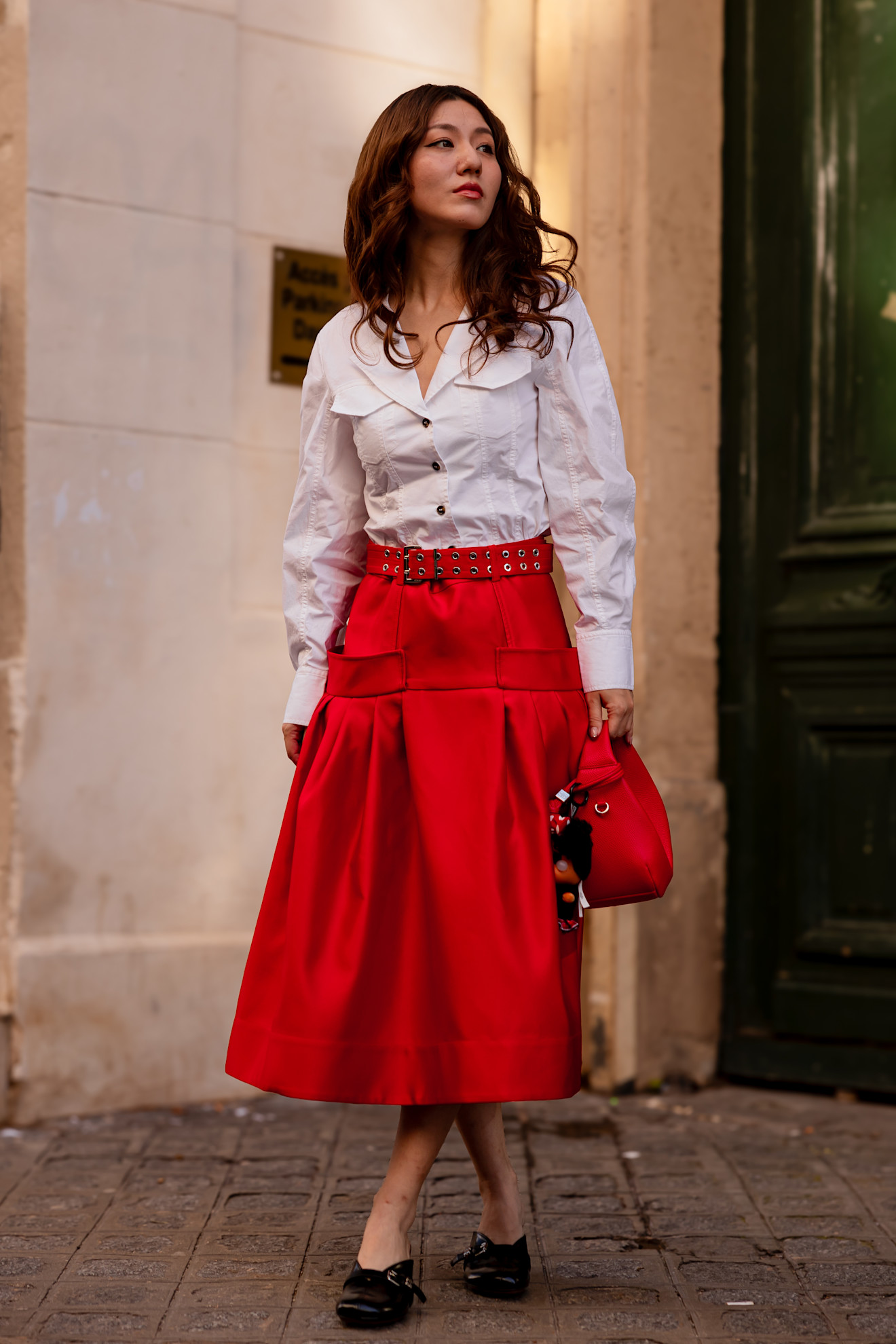 a woman in a red skirt, white shirt, with wavy red hair and a red bag