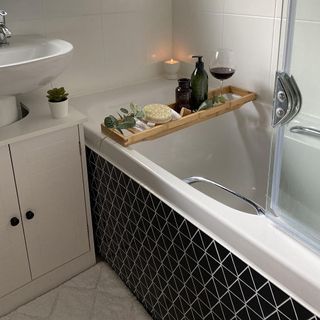 Black tiled bath with white sink and a glass shower screen
