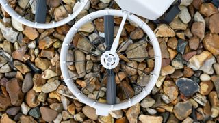 A close up of a propeller with a white rim and black spokes and blades on a stoney background.