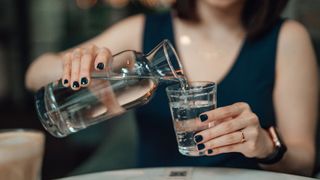 Woman pouring water into glass, enjoying being hydrated, one of the benefits of not drinking alcohol