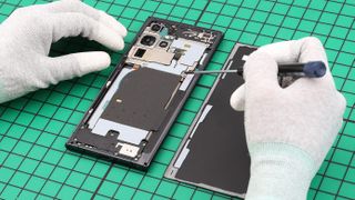 Two hands in white gloves repairing a Samsung phone
