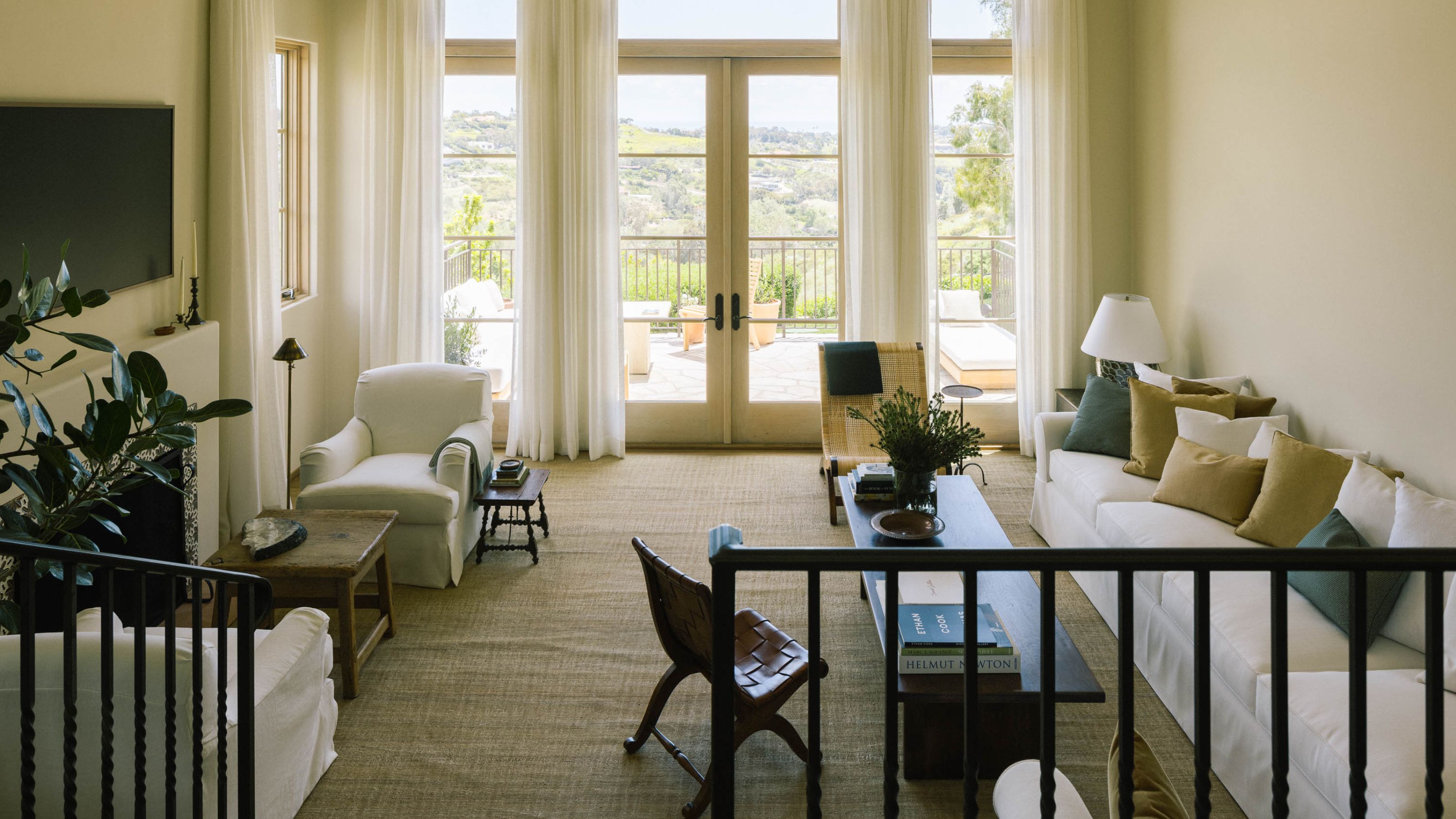 a large open plan airy living room with large patio doors, a large white couch and a fireplace with armchairs