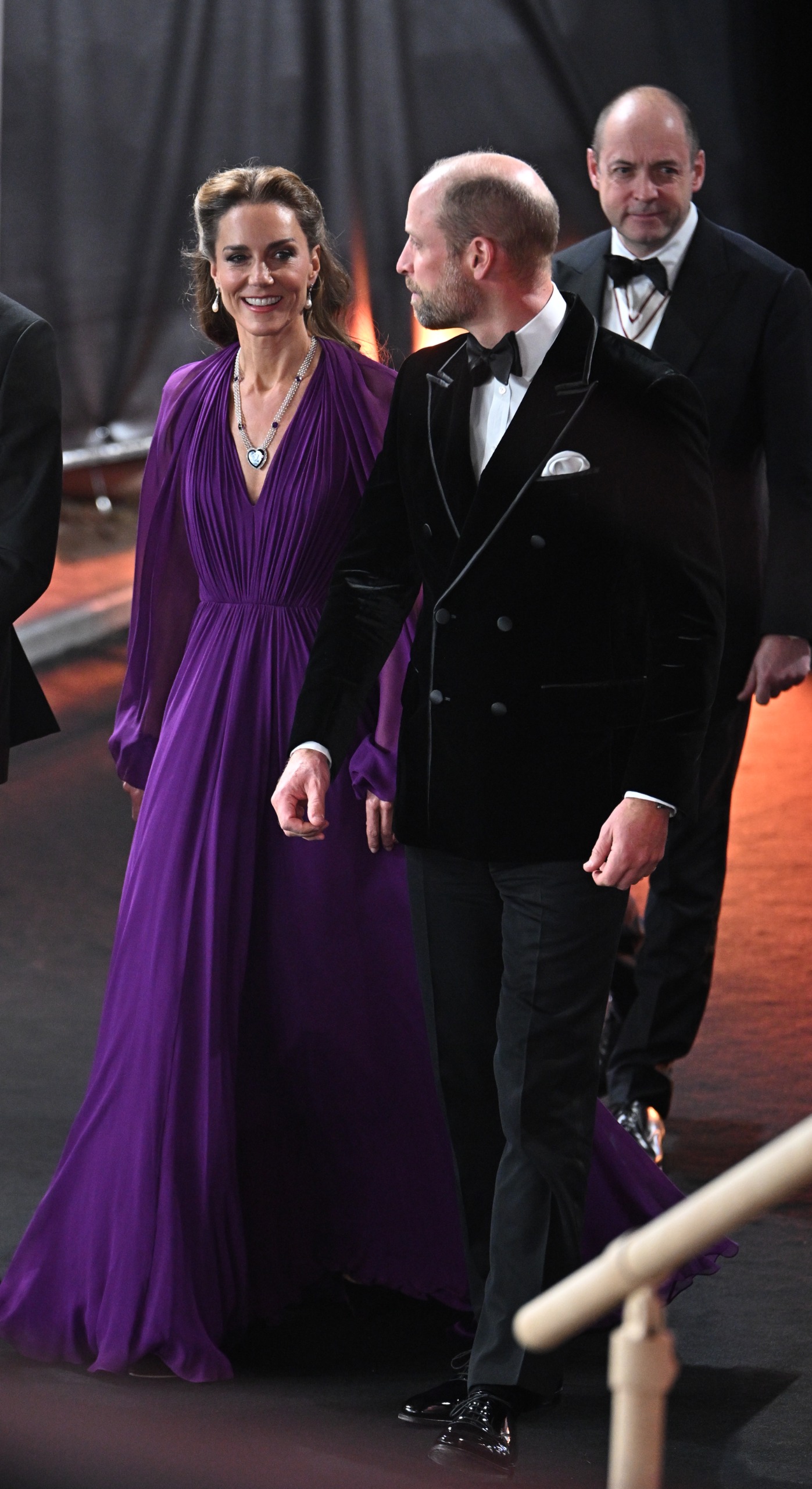 Princess Kate wearing a purple gown walking with Prince William in a tux