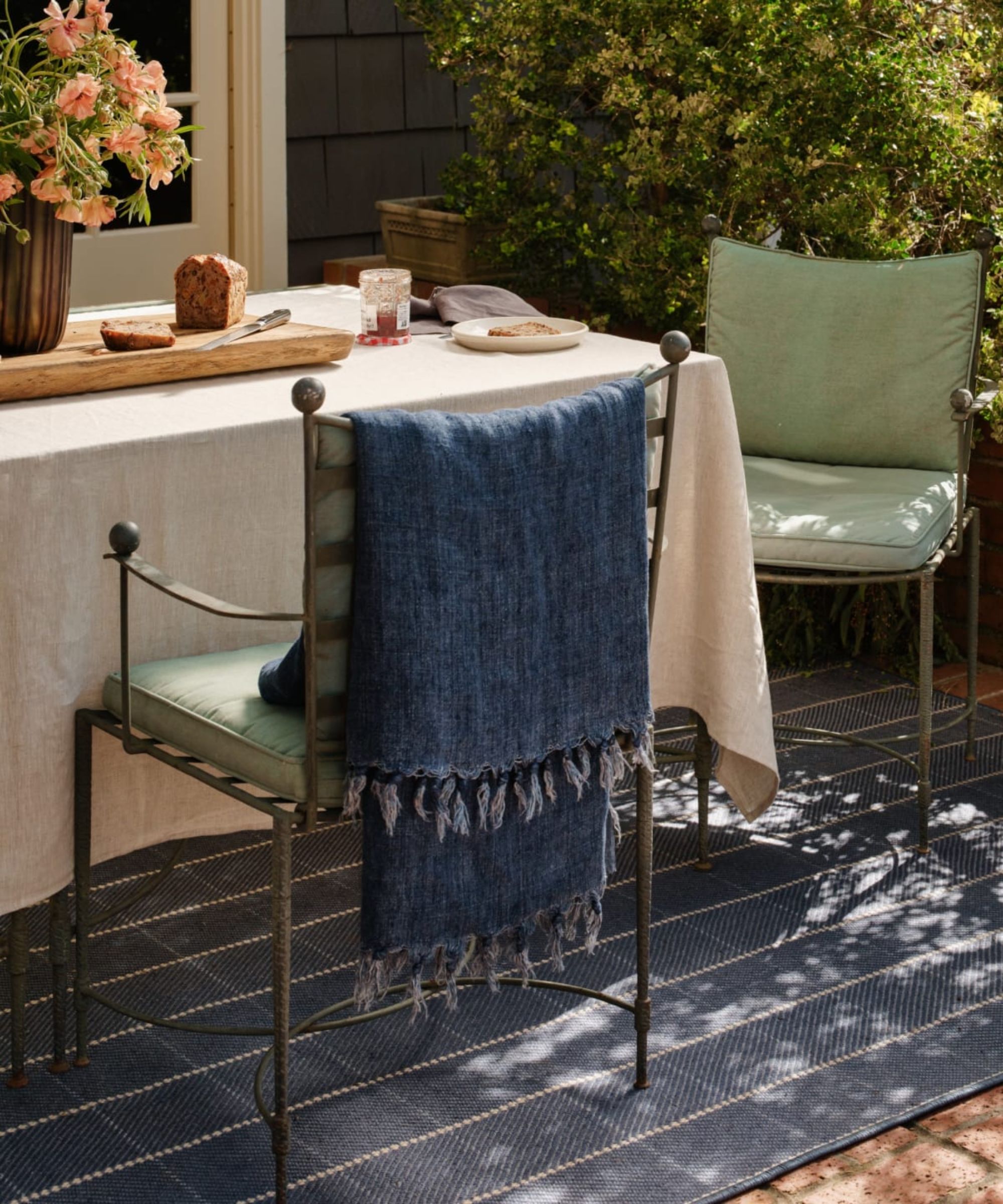 outdoor small patio area with wrought iron dining table and chairs laid for breakfast with green cushions and a blue plaid rug