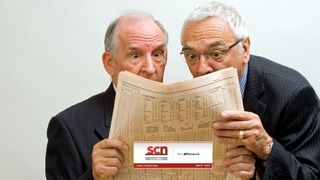 Two old men excitedly read a newspaper. 