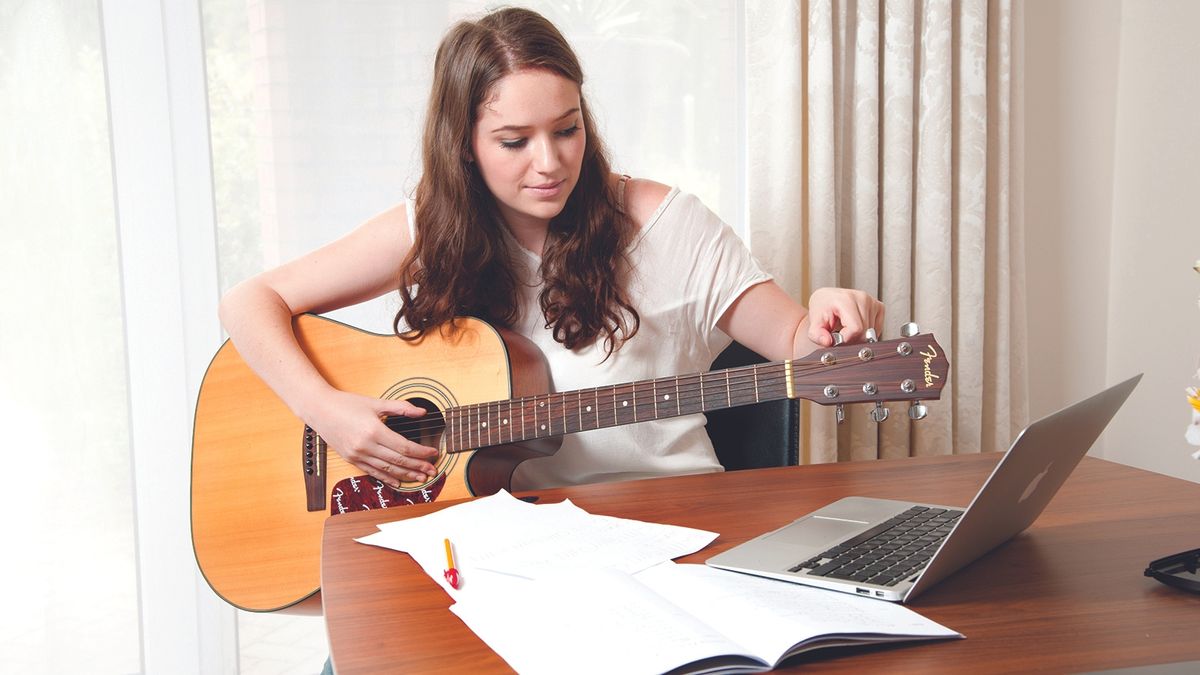 Woman plays acoustic guitar at home with a laptop