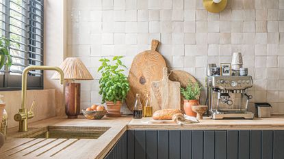 Array of items including wooden chopping boards and a stainless steel coffee machine on a wooden kitchen worktop with beige tiles