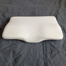 The Kally Sleep Neck Pain Pillow on a grey linen duvet