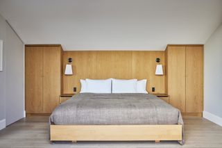 A minimalist bedroom with wooden panelling, grey bedding and white ceiling