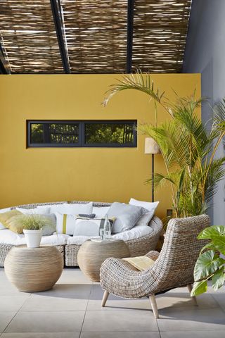 Designing a patio illustrated with yellow and gray walls and rounded wicker garden sofa, chair and coffee tables.