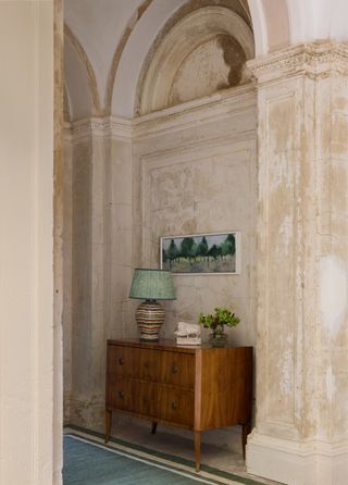 A wooden commode in a large hallway with distressed walls and arched architecture