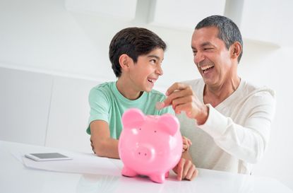 Father contributing to his son's savings by adding coins to his piggybank - home fincances