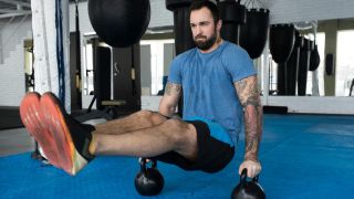 Man performs the L-sit hold using kettlebells