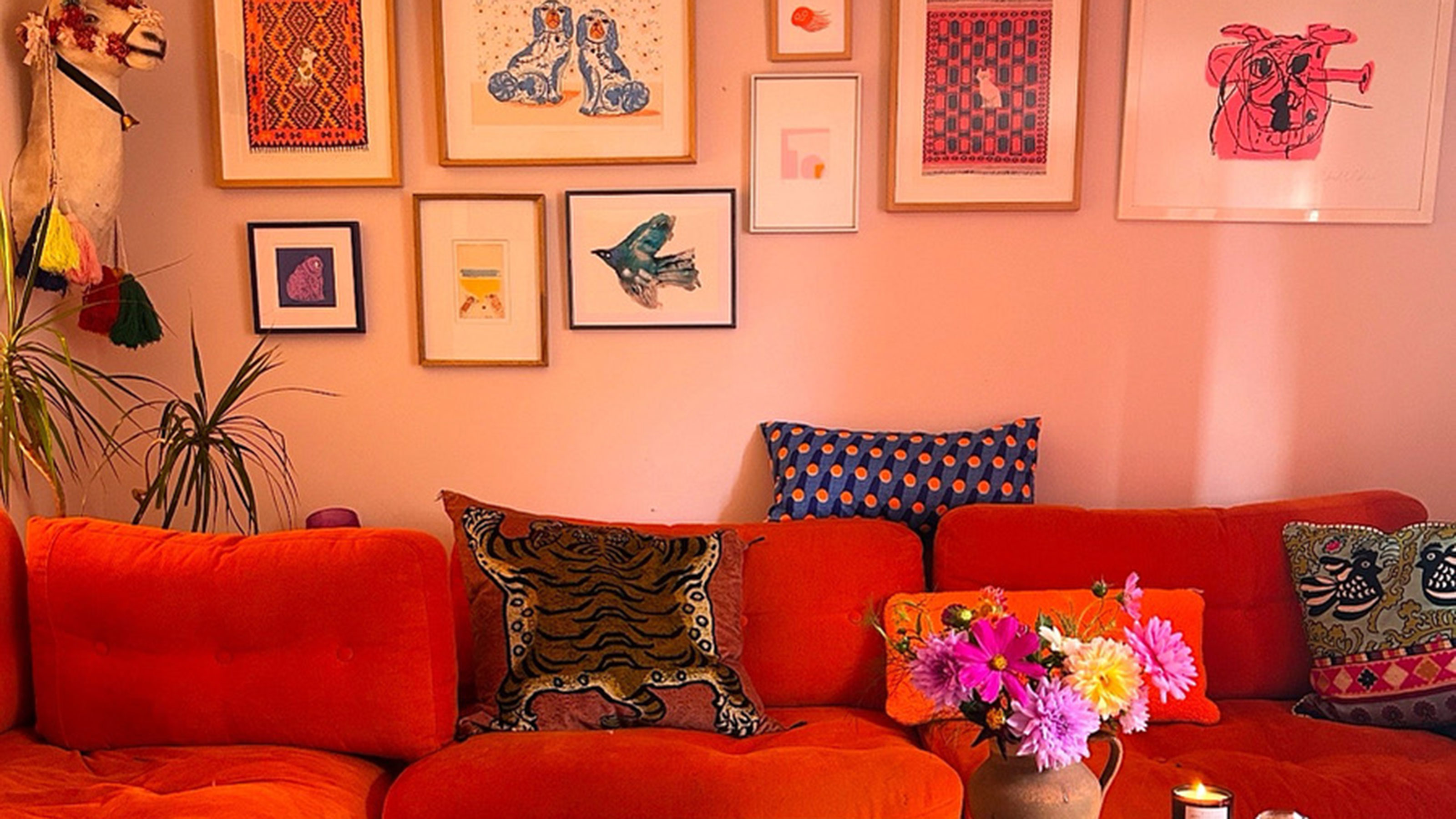 Red sofa with colourful patterned cushions below framed art displayed on pink wall