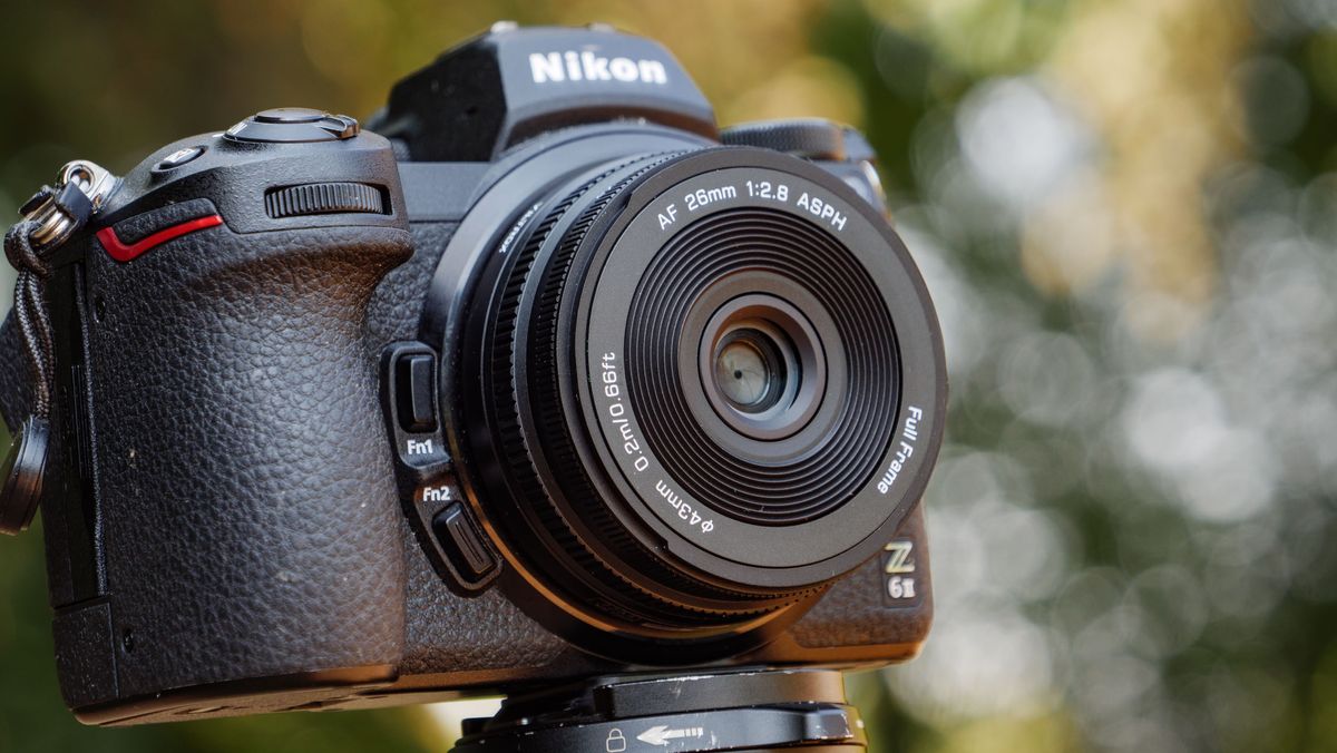 Viltrox AF 26mm F2.8 EVO 'pancake' lens attached to a Nikon mirrorless camera, there's dappled light through a tree behind it