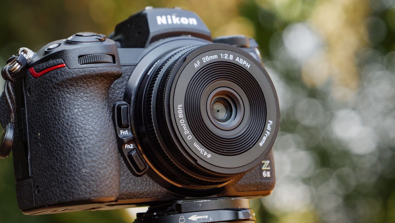 Viltrox AF 26mm F2.8 EVO 'pancake' lens attached to a Nikon mirrorless camera, there's dappled light through a tree behind it