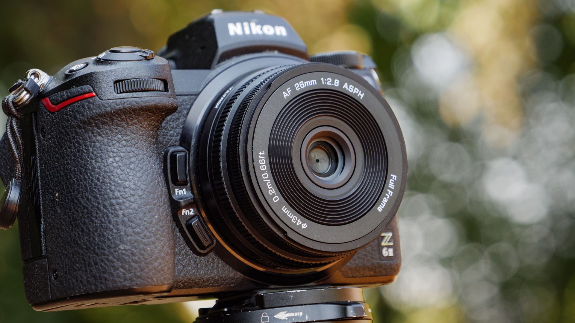 Viltrox AF 26mm F2.8 EVO 'pancake' lens attached to a Nikon mirrorless camera, there's dappled light through a tree behind it