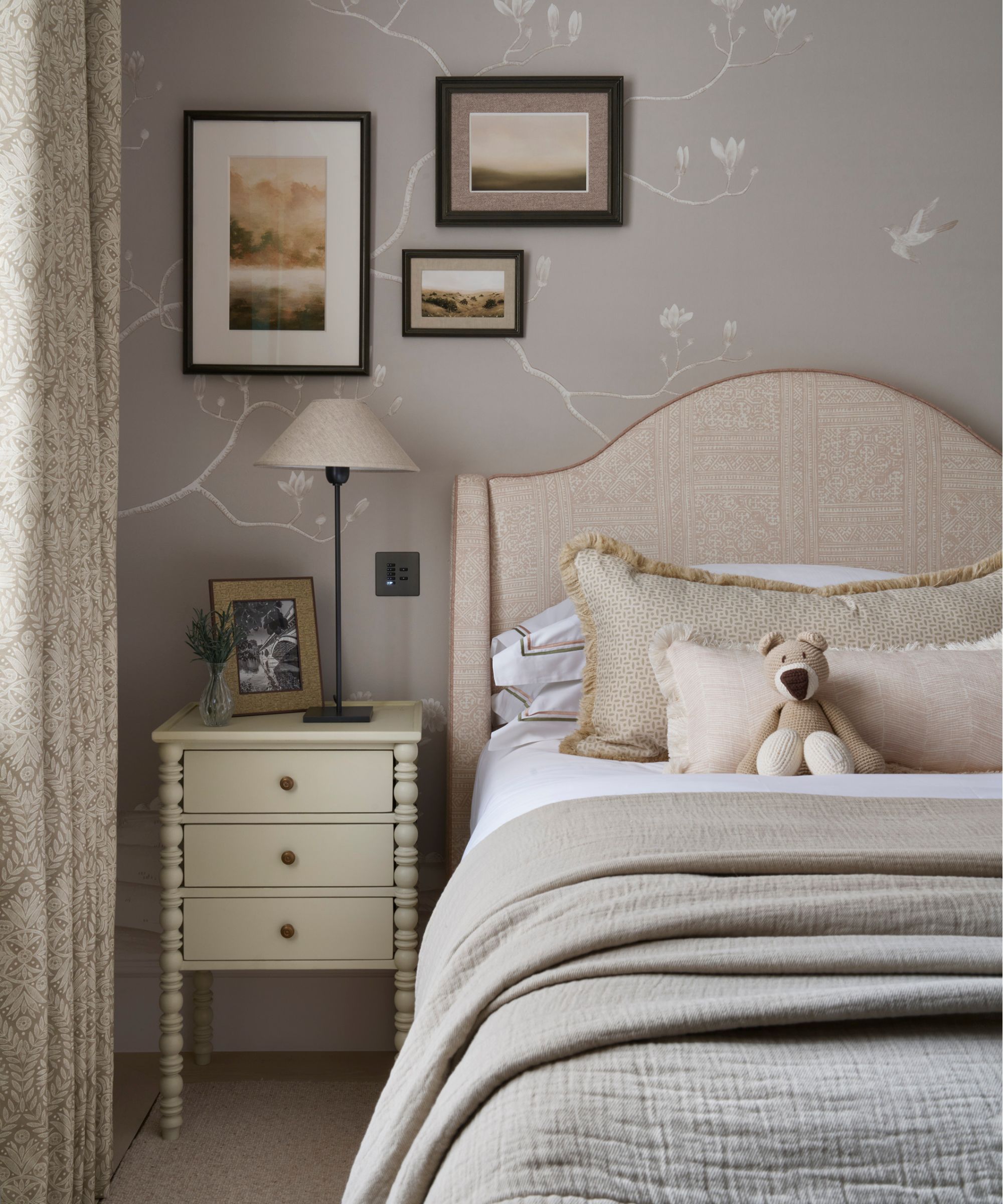 a soft grey floral wallpapered girls bedroom with a small neutral bed, bobbin-style nightstand and soft landscape artwork on the wall